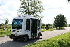 white small automated electric shuttle, pathway, green grass, trees